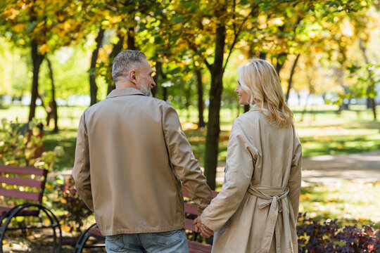 Side view of carefree middle aged couple holding hands while walking in park.
