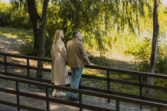 Side view of middle aged couple looking away while standing on bridge in spring park.