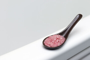 Himalayan salt in a porcelain spoon on the side of a white bathtub