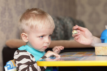 Mom feeds the child from a spoon at the children's table