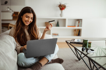 Smiling millennial mixed race woman shopaholic typing on laptop, using credit card, enjoy online...