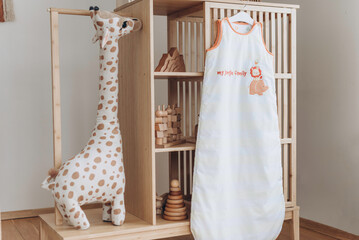 Baby sleeping bag with hanger in child room interior. Kid clothes. Copy space.