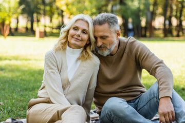 portrait of charming middle aged couple sitting together in green park during springtime.