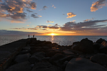 Fototapeta na wymiar Ein schöner Sonnenuntergang über dem Meer und Angler stehen am Strand und Fischen