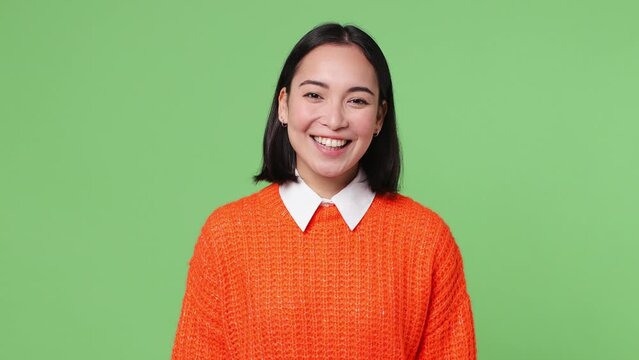 Beautiful happy cheerful fun young woman of Asian ethnicity 20s she wear knitted orange sweater posing looking camera smiling isolated on plain pastel light green color wall background studio portrait