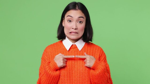 Hesitant fun shy young woman of Asian ethnicity 20s she wear orange sweater feels doubtful spreading hands say oops ouch oh omg i am so sorry isolated on plain pastel light green color wall background