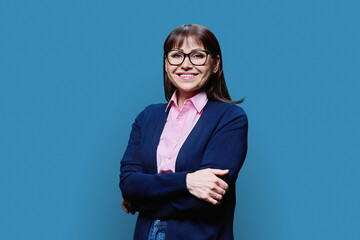 Positive middle aged woman posing over blue studio background
