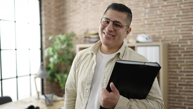 Young hispanic man business worker holding binder standing at office