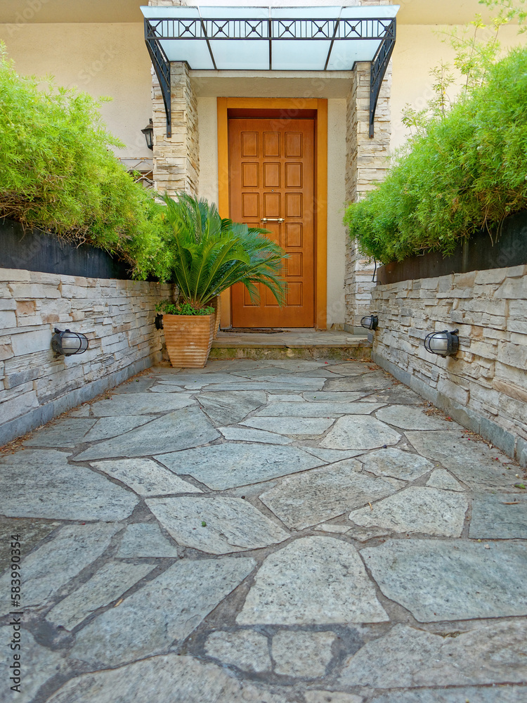 Wall mural a stone paved corridor through the garden of a family house with a natural brown wood door. athens, 