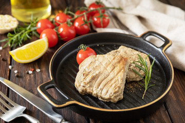 Cooked juicy tuna steak  with spices, tomatoes and rosemary on a stone plate. Restaurant food. Seafood. Rustic style.