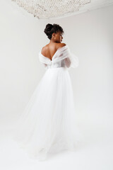 Fototapeta na wymiar Model with dark skin in a white dress. Wedding make-up, wedding hairstyle. African American model posing in a white wedding dress.