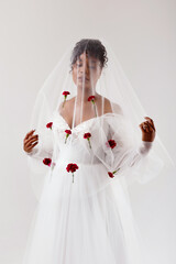 An African American woman in a wedding dress looks through a veil. The wedding veil is decorated with red flowers.