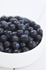 Fresh raw Patagonian Calafate berries (lat. Berberis heterophylla) in white bowl, photographed on white wood (Selective Focus, Focus one third into the berries)
