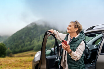 Beautiful happy gray-haired mature traveling by car and using smartphone for navigation. Active pensioners concept