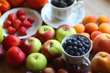 Berries in vintage porcelain dishes, other healthy fruit and vegetable on wooden table. Selective focus.