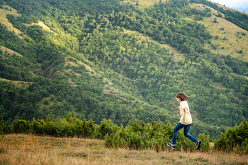 Fototapeta na wymiar 10 years girl running across a summer meadow against the backdrop of green hills and mountains. Youth and freedom, harmony with nature, happy childhood, summertime