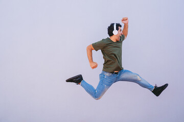 Middle-aged man wearing headphones doing the jump of hurdles race on white background. Copy space.