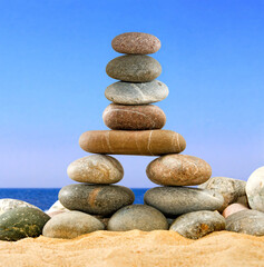 Fototapeta na wymiar zen pyramid of stones on the sand against the background of the sea and blue sky
