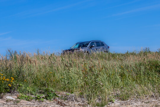 The car is driving by the meadow in the sun. The background is blue sky.