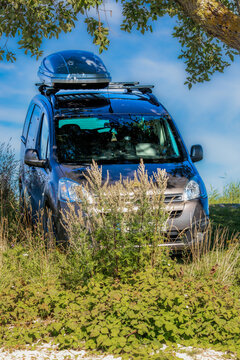 The car is standing under a bush in the sun. The background is blue sky.