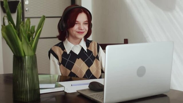 A girl with red hair, a teenager of 15 years old, works at a laptop computer, online training, a conference. Online learning concept