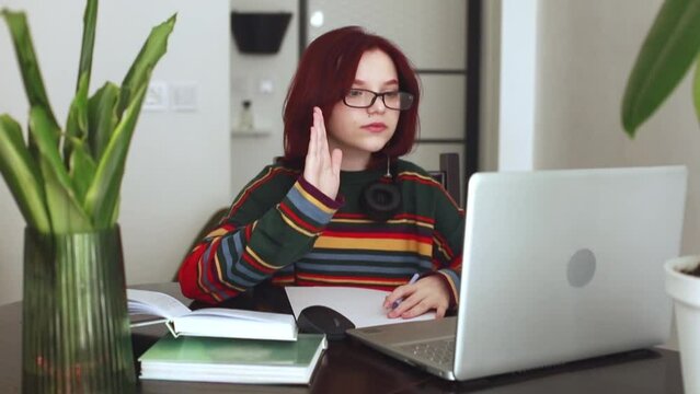 A girl with red hair, a teenager of 15 years old with glasses, works at a laptop, online learning, a conference. Online learning concept