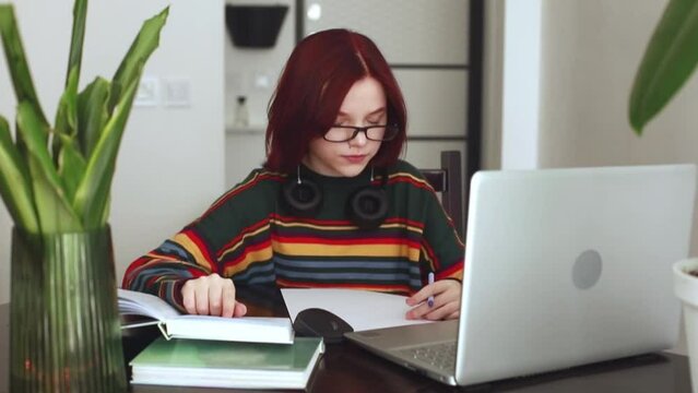 A girl with red hair, a teenager of 15 years old with glasses, works at a laptop, online learning, a conference. Online learning concept