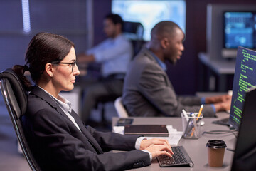 Side view portrait of serious businesswoman using computer at workplace in high tech IT security office