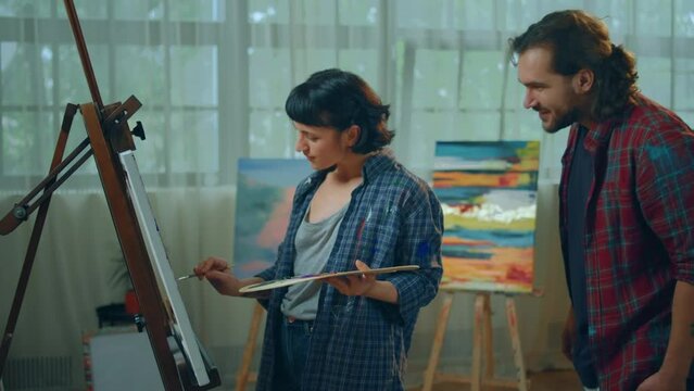 Concept of art education two happy and charismatic artist man and woman speeding time in their studio woman creating a beautiful picture using the oil colour from the palette