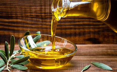 Organic olive oil pouring from carafe  into glass bowl