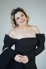 A smiling woman in a black dress poses on a white background.