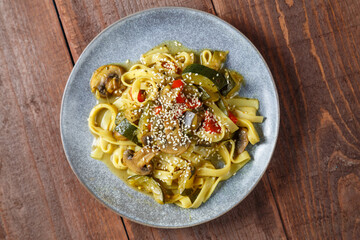 Gray plate with udon vegetables and gibi sprinkled with sesame seeds on a wooden table. save a place