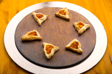 Triangular gomentashi cookies for the holiday of Purim on a blackboard are laid out on a round board on a light table.