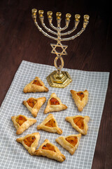 Homemade gomentashi cookies for the Jewish holiday of Purim on a checkered napkin next to the menorah.