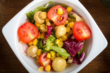 Vegetable salad with champignon corn and cherry tomato with avocado in a white plate.