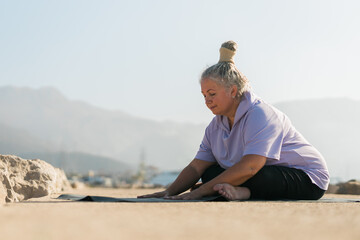 Mature woman with dreadlocks working out doing yoga exercises on sea beach - wellness well-being and active elderly age concept