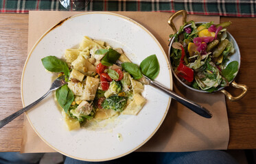 Pasta with chicken ,sauce and basil on a plate and salad with vegetables on dinner in restaurant. Helathy food for eating. 