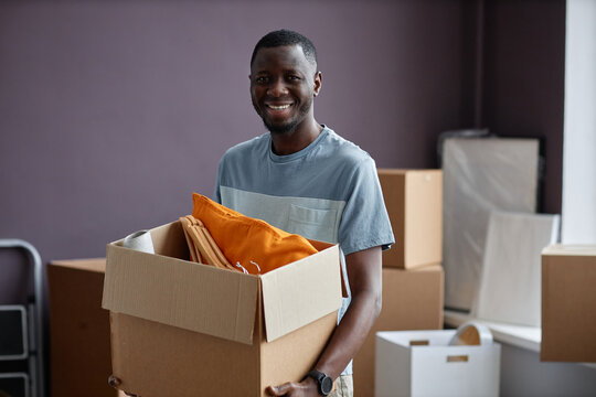 Portrait of African American man smiling at camera carrying cardboard boxes in new home