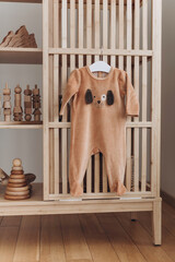 Baby bodysuit with dog face on hanger, beige background. Cute children's clothes and wooden toys, pyramid in nursery room. Copy space. Scandinavian child room