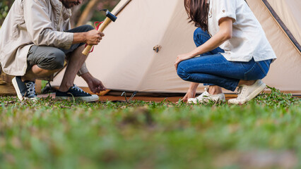 Asian couple pithing tent camping outdoors. Happy friends setting up tent campsite. Travel and camping concept