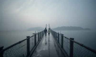 Foto auf Acrylglas  a couple of people walking across a bridge on a foggy day.  generative ai © Nadia