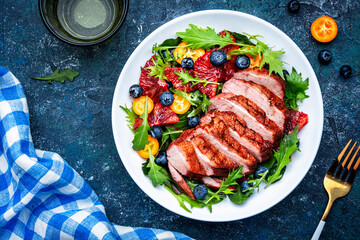 Duck salad with grilled breast with red orange, kumquat, blueberry and chard, frisse, mizuna and arugula leaves on blue table background, top view