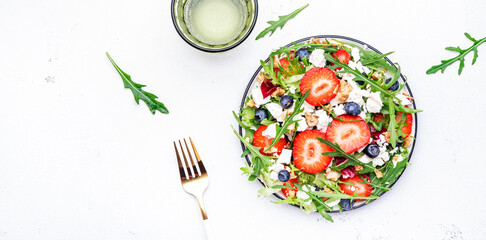Strawberry and herbs healthy salad with arugula, blueberries, soft white feta cheese and walnuts, white kitchen table, place for text. Fresh useful dish for healthy eating