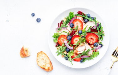 Strawberry, grilled chicken fillet and herbs healthy salad with arugula, blueberries and walnuts, white kitchen table, place for text. Fresh useful dish for healthy eating