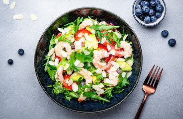 Strawberry, shrimp and herbs healthy salad with arugula, avocado and almond slices, gray kitchen table. Fresh useful dish for healthy eating