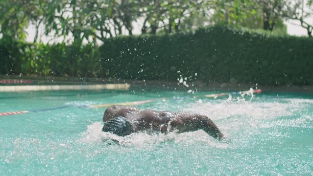 Professional black swimmer in goggles and cap practicing butterfly stroke in outdoor pool while training on summer day