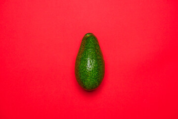 Organic green avocado top view on a red background. Cool minimal flat lay, copy space 