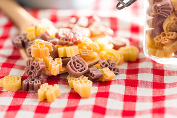 Pasta of various scary shapes. Uncooked halloween pasta in spoon on checkered tablecloth.