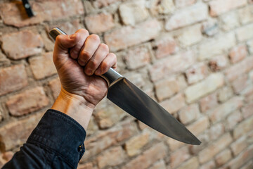 Agressor holding steel metal knife with brick wall background