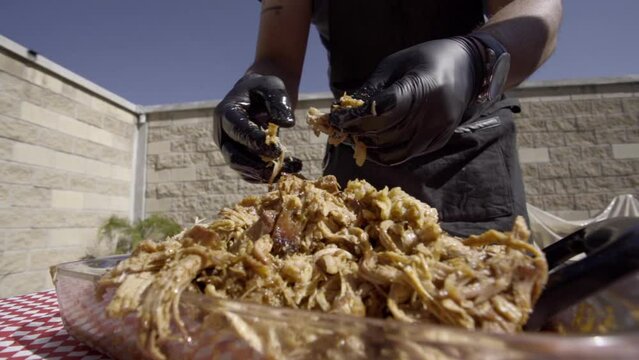Hands with black gloves, shred the meat of a Pulled Pork just out of the oven.